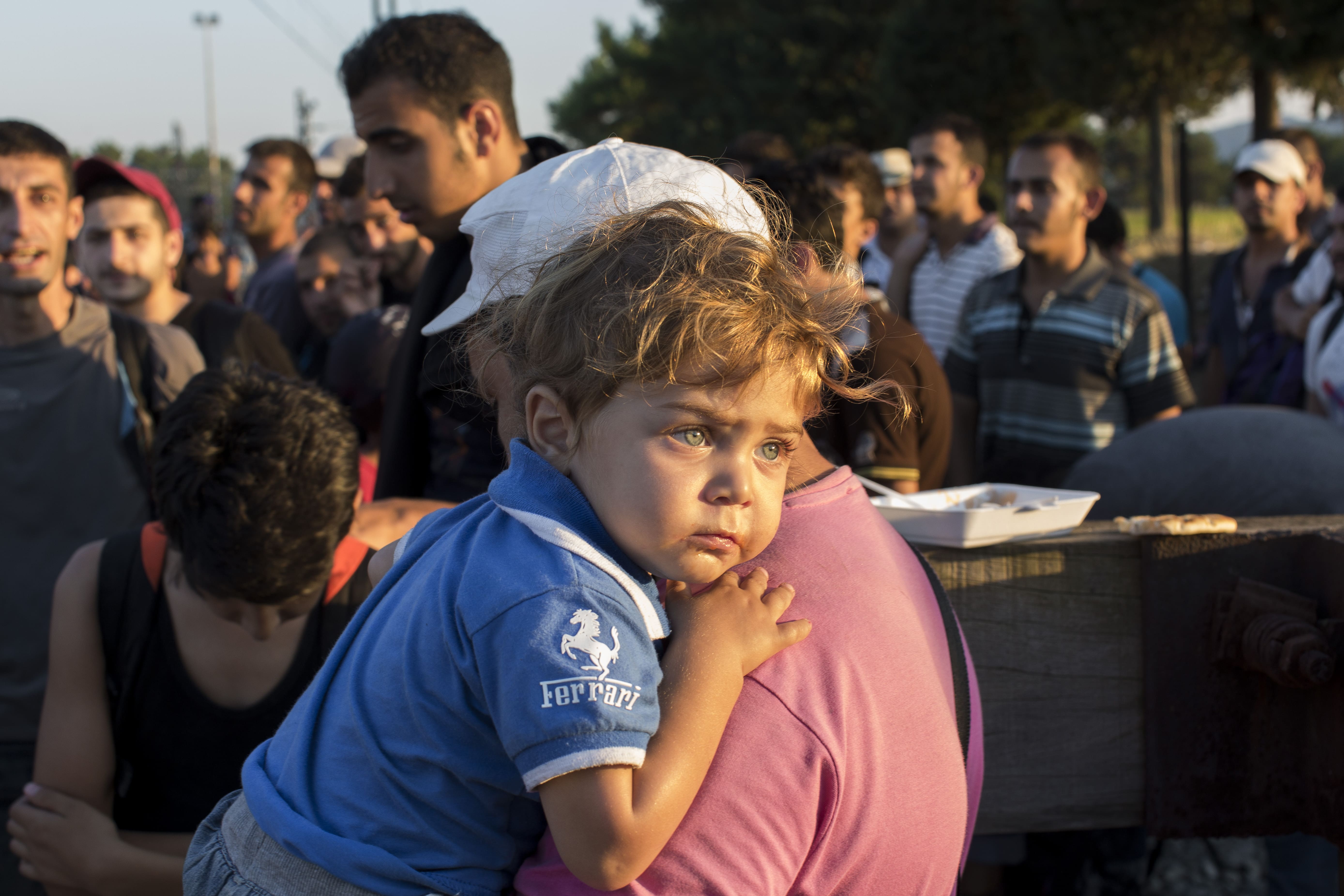 A Syrian refugee holds his son as they wait to move closer to crossing the border between Greece and the Former Yugoslav Republic of Macedonia.