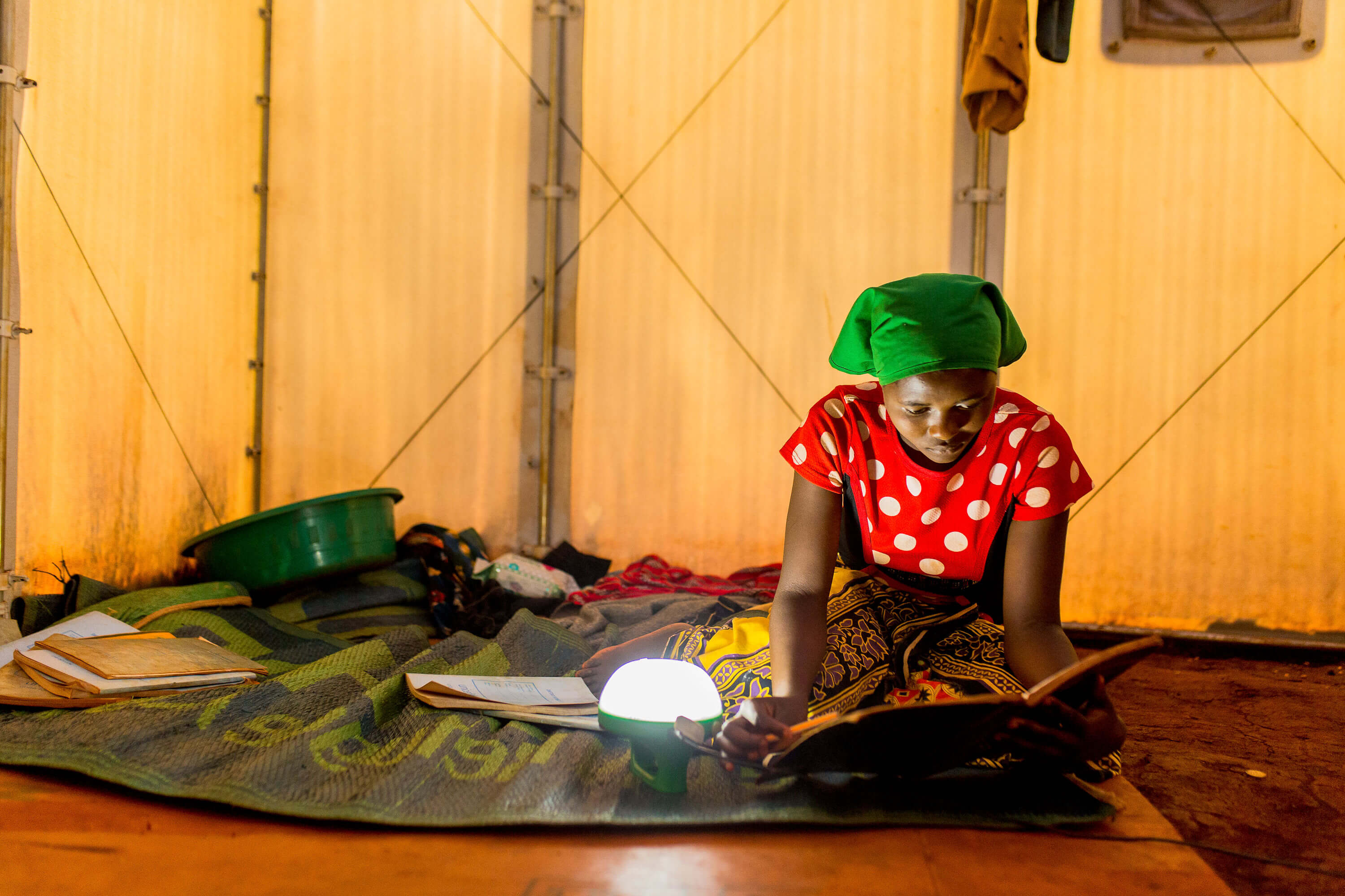 A refugee woman in Tanzania studies by lamplight.