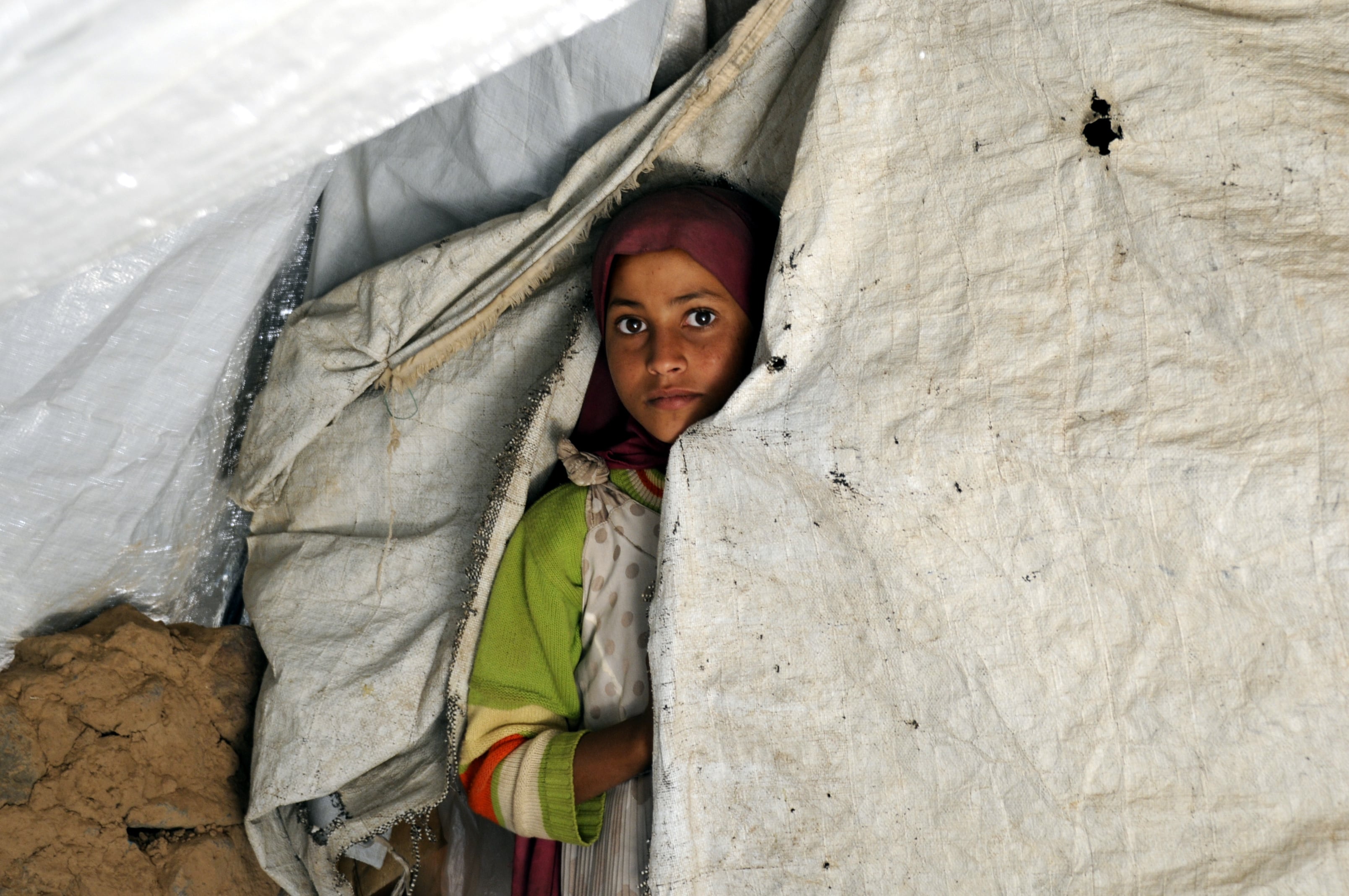 Lujain Qasim, 11, looks through an opening in her family's tent at the Dharawan settlement