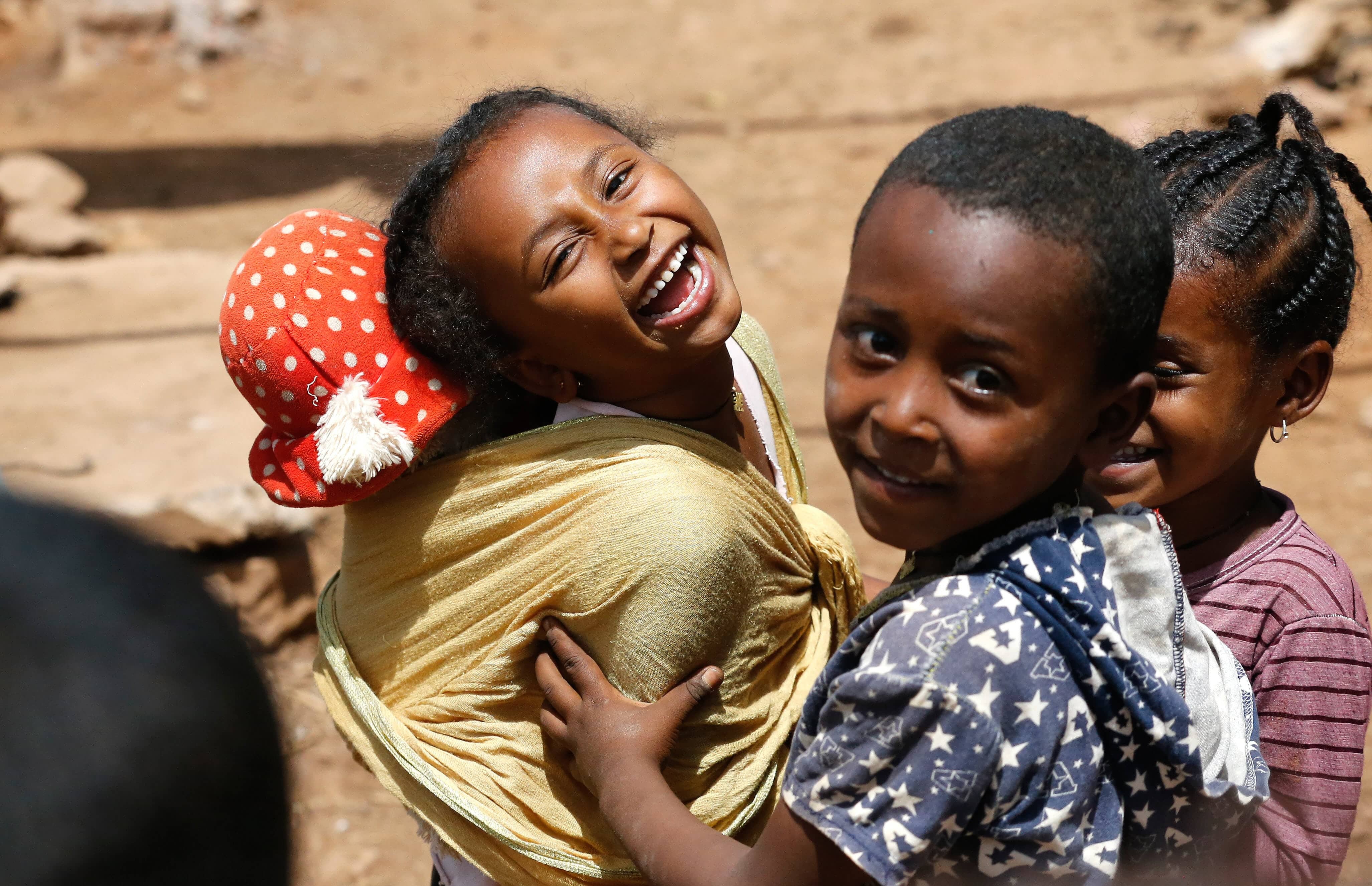A young girl, carrying her doll on her back, laughs at the camera at Kakuma refugee camp in the north-westerm region of Kenya.