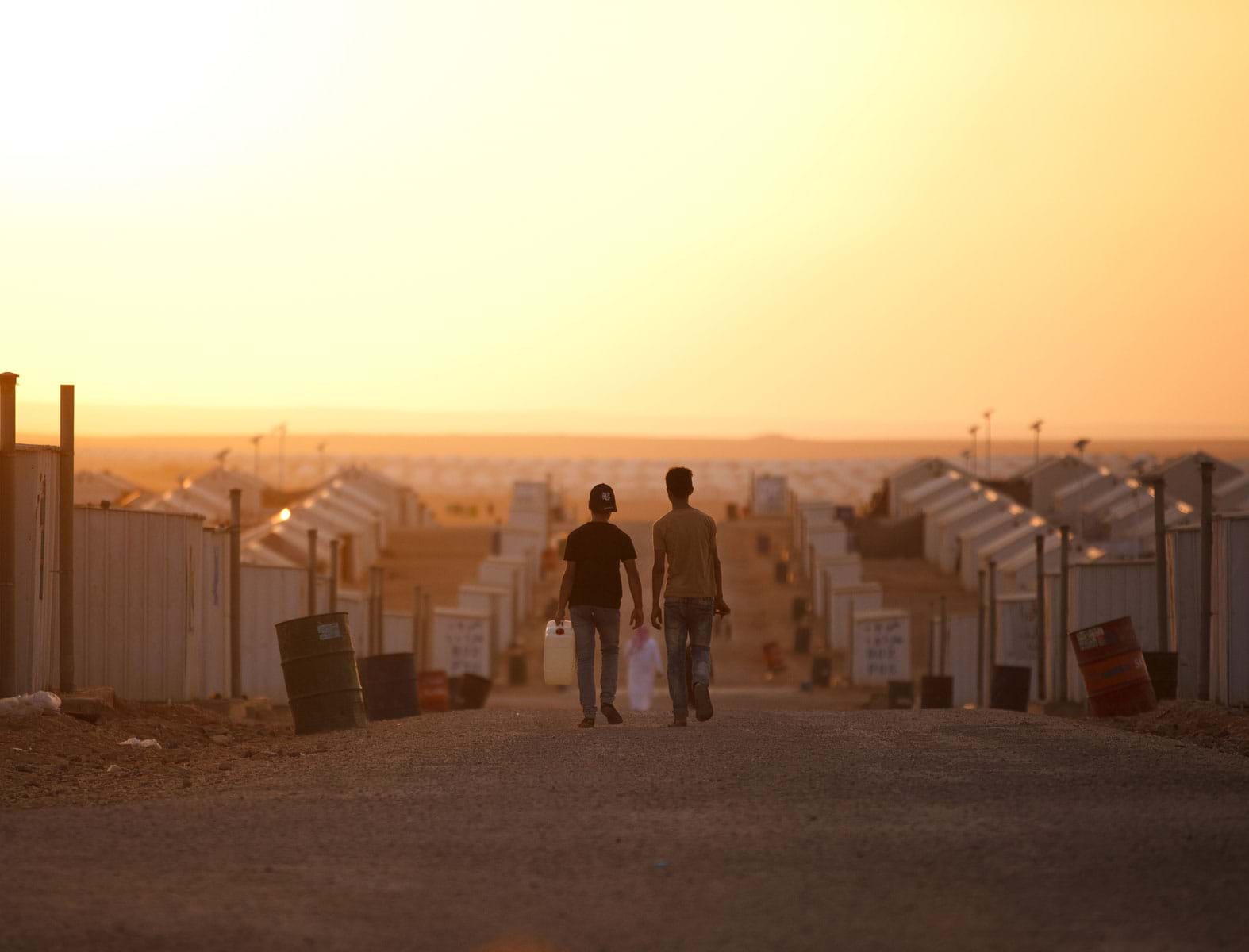 Two young refugee boys walking through a village of temporary tent accommodation