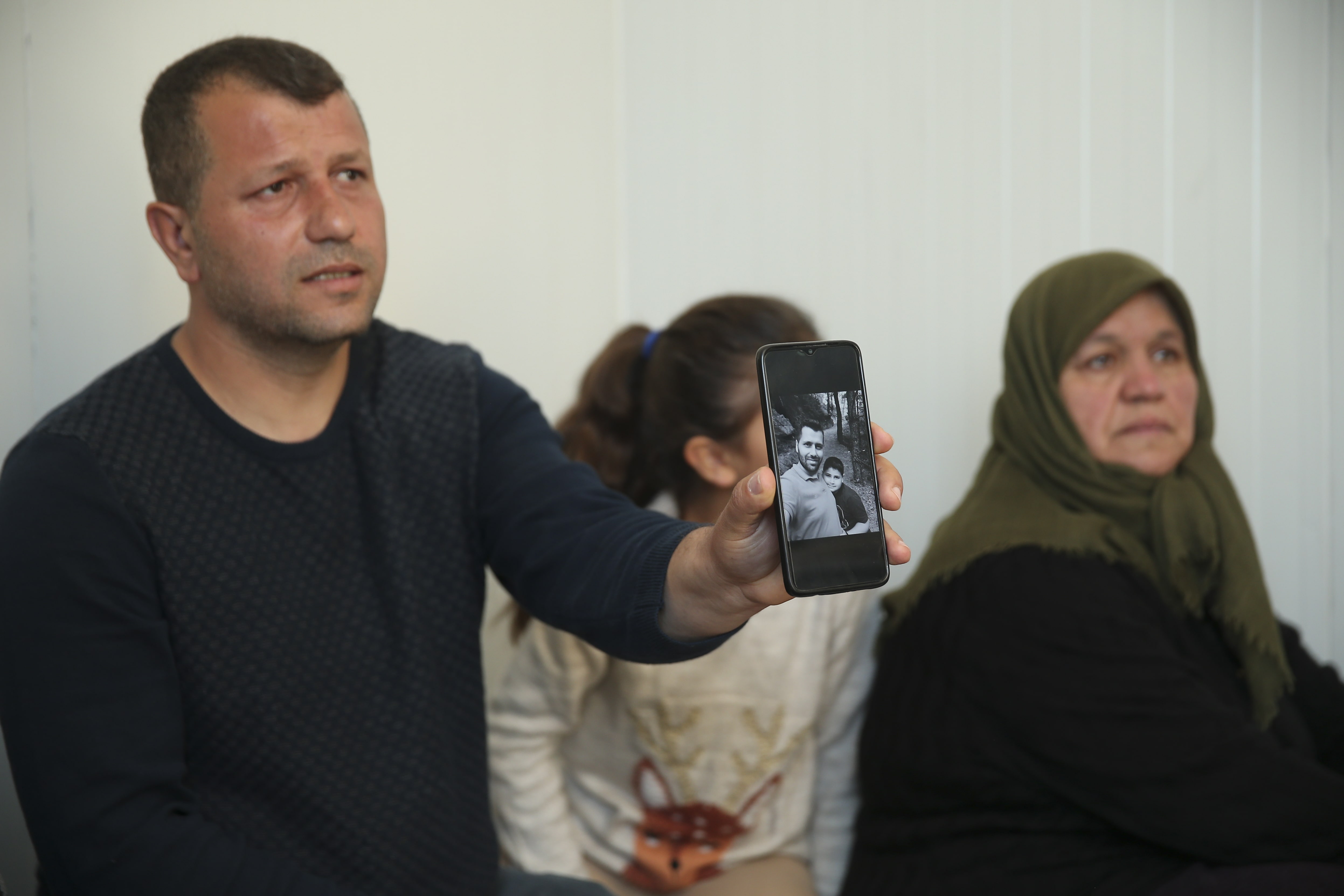 Ahmet Erkan, with his daughter and mother, shows a photograph of his brother and nephew who died when their building collapsed during the devastating February earthquakes.