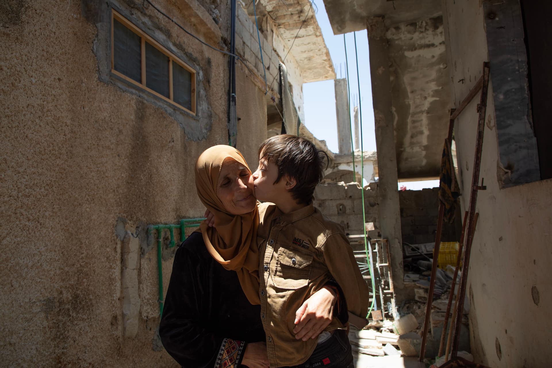 Awatef, 48, carries her youngest child, Amir—who has Down syndrome—inside their war-damaged home after returning from Jordan