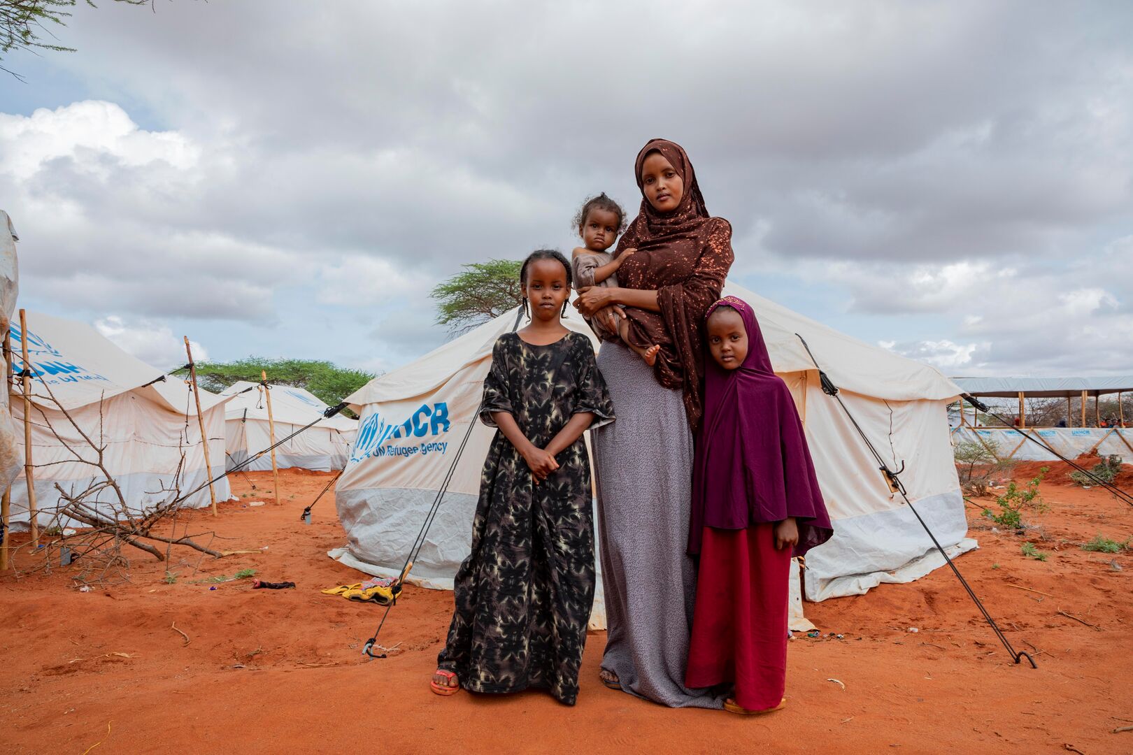Hafsa stands in front of her shelter with her three daughters