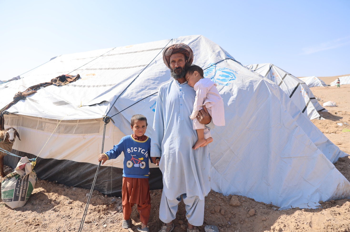 Nisar, 40, and two children stand outside a UNHCR tent. They survived earthquakes in Herat, Afghanistan, in October which affected more than 7,000 families.