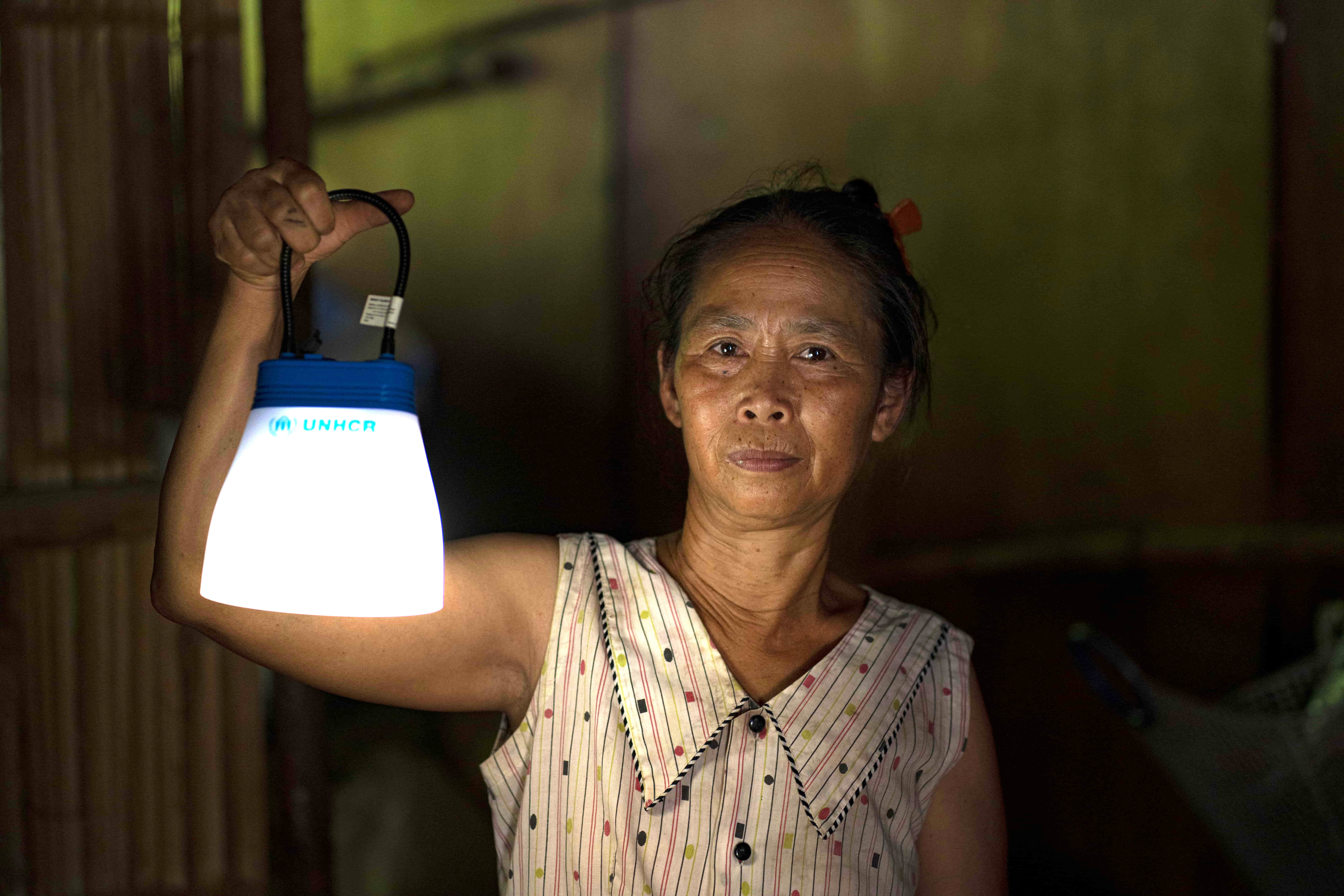 A woman holds up a solar lamp in a dim shelter in Myanmar. The country is experiencing a deepening humanitarian crisis.